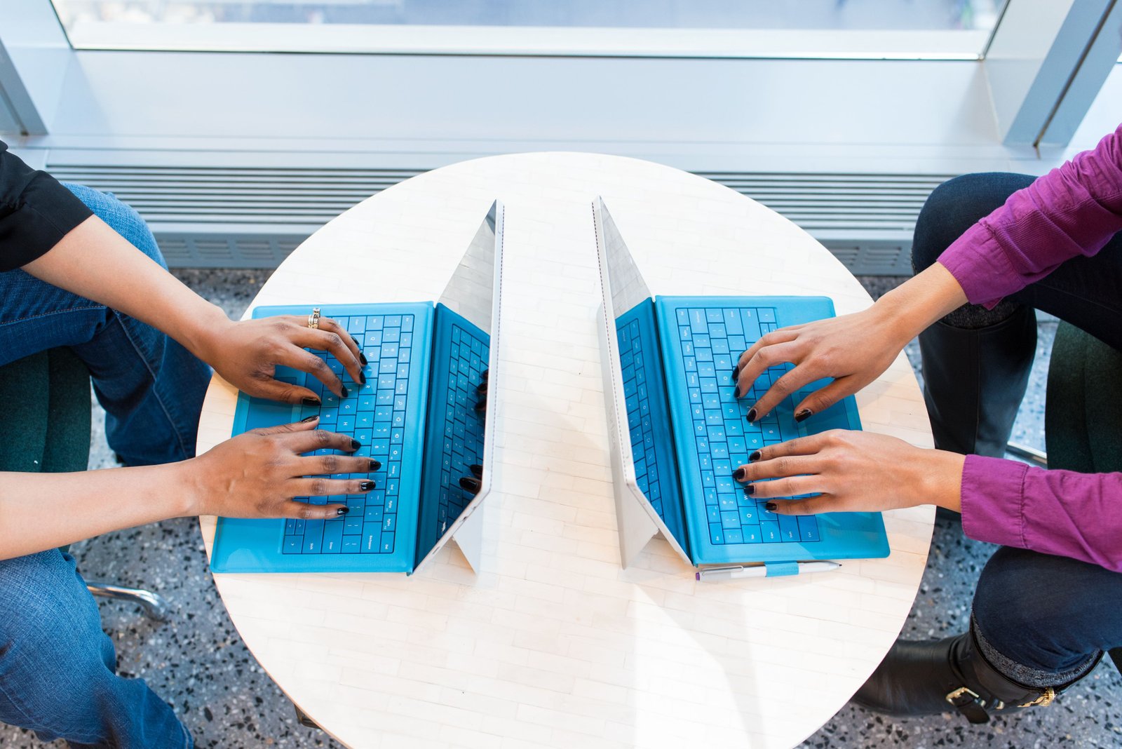 Two people working on blue laptops at a round table, focusing on teamwork and technology.