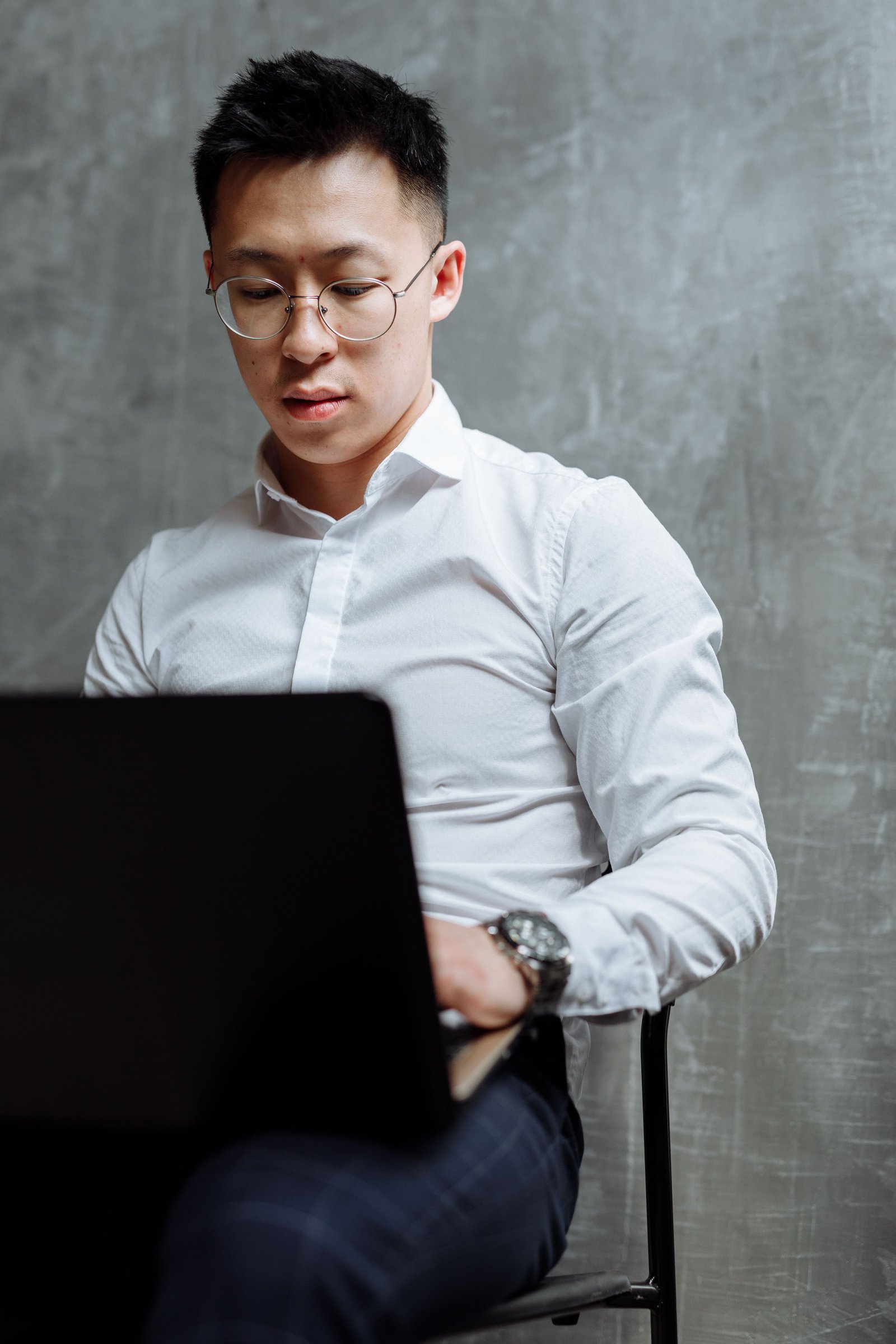 Focused businessman using a laptop indoors, wearing glasses and a white shirt.