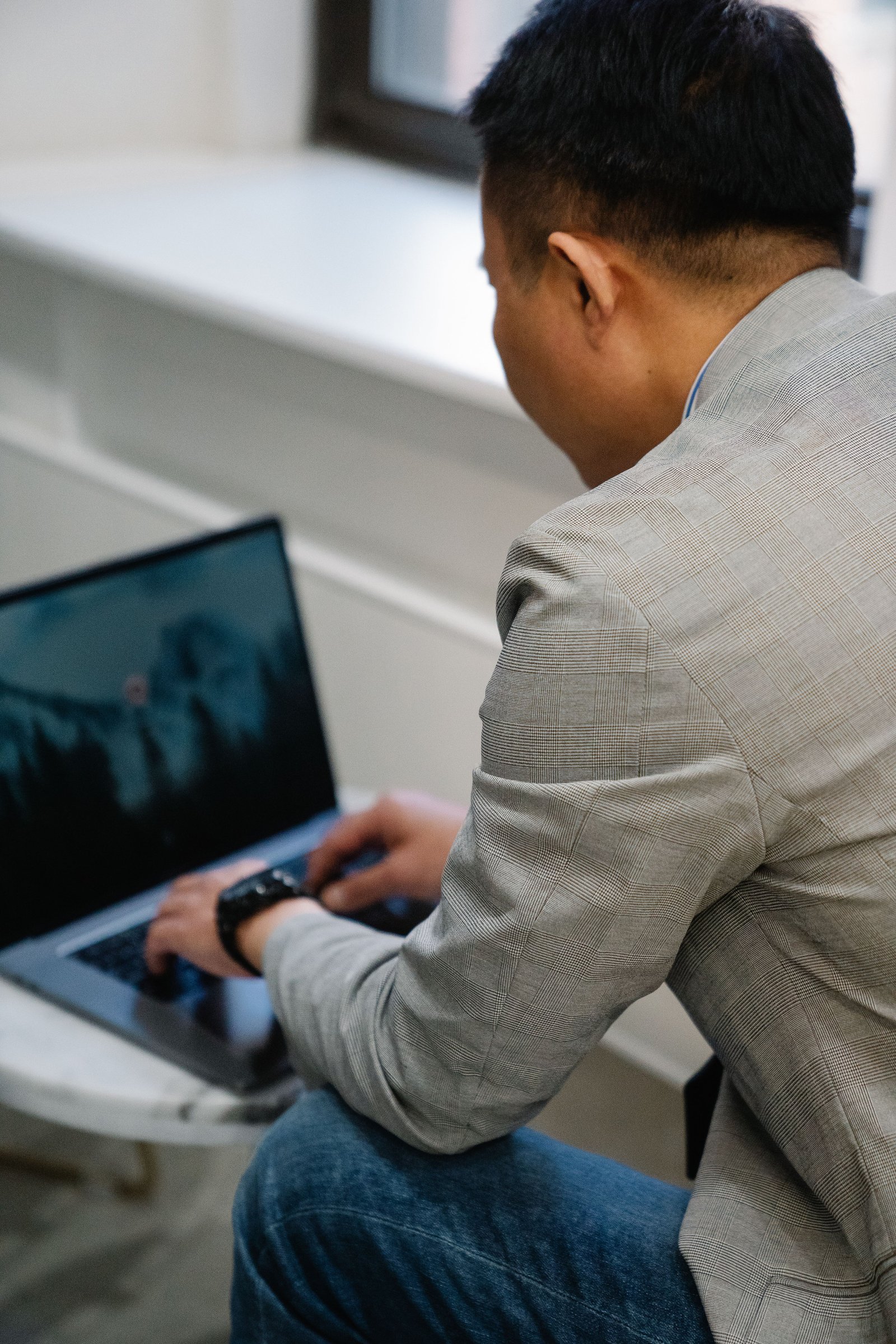 Man in a suit typing on a laptop indoors, focused and working on a modern setup.